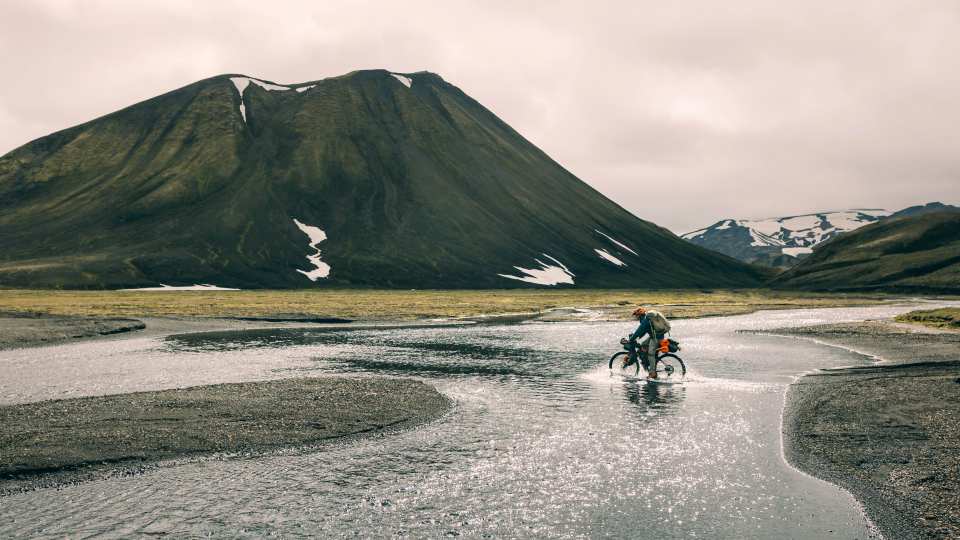 A bikepacker embraces soggy socks as he crosses a shallow river cycling the Kjolur Route in Iceland during the summer months
