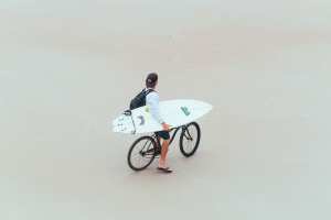 Man with surfboard on bike on Daytona Beach