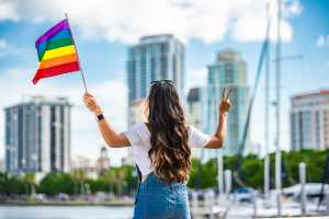 Woman holding up pride flag in front of city