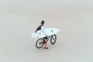 Man with surfboard on bike on Daytona Beach