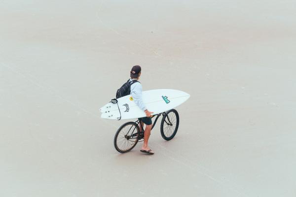 Man with surfboard on bike on Daytona Beach
