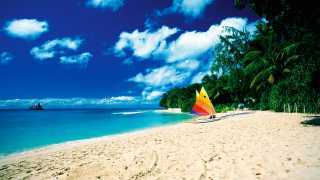A beach in Barbados with a colourful sailboat