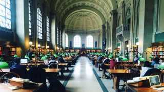 The inside of Boston Public Library, with lamps lit and people at work