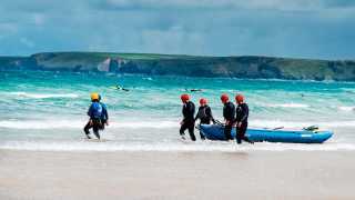 A group walk their raft into the Cornish sea