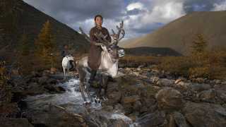 A mother and child ride reindeer on the Mongolian steppe