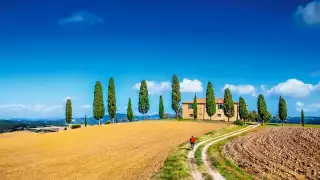Classic panorama view of scenic Tuscany landscape with farmhouse and male cyclist on a country road on a beautiful sunny day in summer, Italy