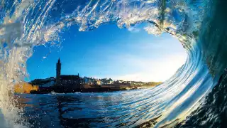 A wave in Porthleven framing the Cornish town's skyline