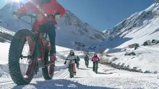 A group of five rides fat bikes along the marked tracks in the snow-covered valley