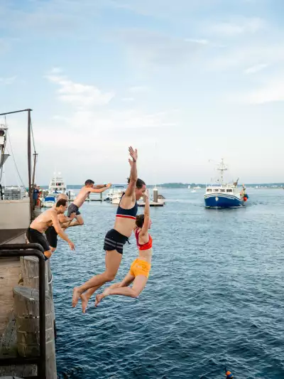 Members of Portland&rsquo;s Old Port Pub Run cool off after a group run, jumping from the pier into the harbour as fishing boats return to shore