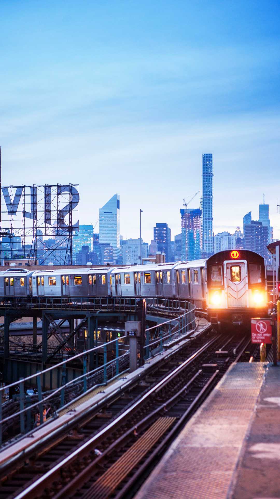 A 7 train rides the New York subway tracks, in front of the twinkling Manhattan skyline at dusk