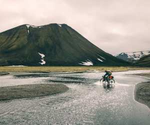 A bikepacker embraces soggy socks as he crosses a shallow river cycling the Kjolur Route in Iceland during the summer months