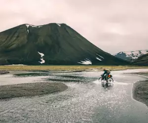 A bikepacker embraces soggy socks as he crosses a shallow river cycling the Kjolur Route in Iceland during the summer months